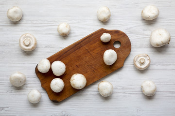 Champignon mushrooms on wooden board over white wooden surface, top view. From above, overhead.