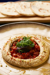 Vegetarian Hummus with harissa sauce and pistachios close-up. Delicious diet food with pita bread on wooden cutting board