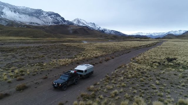 Aerial drone scene of Andes mountains, in Mendoza, Argentina. Patagonia steppe landscape. Camera going backwards over a gravel lonely road tracking van with trailer, motorhome. Campanario mountain.
