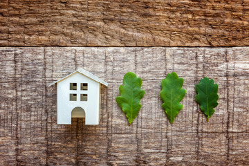 Miniature white toy model house with green oak leaves on wooden backgdrop. Eco Village, abstract environmental background. Real estate mortgage property insurance dream home ecology concept