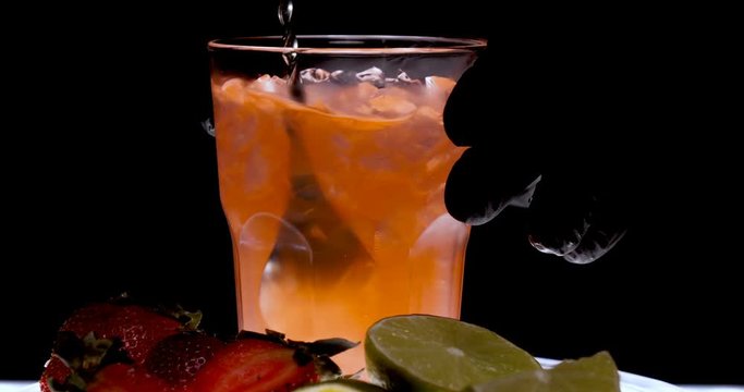 Orange alcohol cocktail in a glass, black background, strawberry, lime, black background, cold drink, ice, fresh.