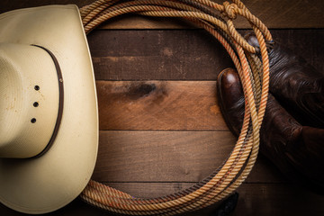 A cowboy hat, lariat rope and boots on a wooden plank background