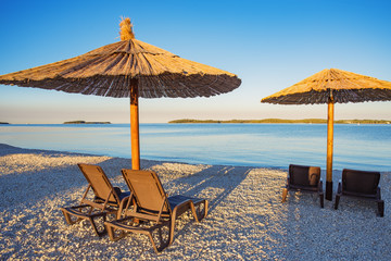 Sonnenschirm mit Liegestuhl am Strand. Morgens am Meer bei Sonnenaufgang