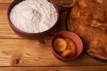 A bowl with flour and apricot cake on a wooden background