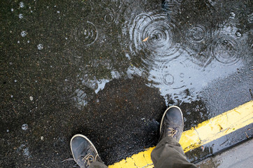 Rainy weather. Male legs in sneakers or boots walking through the rain puddle on the asphalt road,...