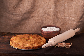 On a dark wooden table, fashionable bakeries, a bowl with flour, apricot cake and tools stand on table