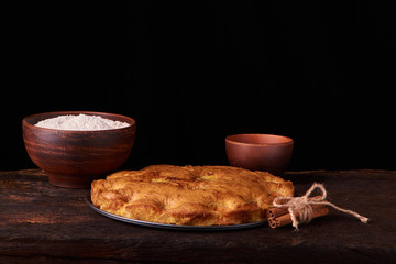 On a dark wooden table american apricot pie, ingredients and tools on black background