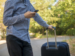 young teenage man in casual traeling in the city street with baggage and using phone