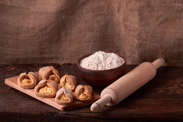 Composition of tasty cottage chees cookies on chopping board with bowl flour and rolling pin. on rustic background