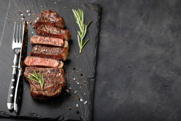Closeup ready to eat steak new York beef breeds of black Angus with herbs, garlic and butter on a stone Board. The finished dish for dinner on a dark stone background. Top view with copy space