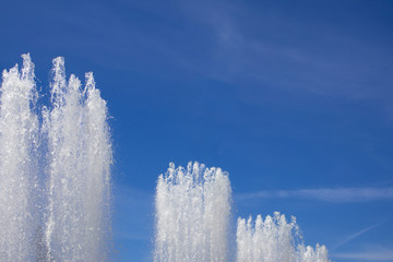 Tops of large fountain jets gushing upwards against blue sky, may be used as background