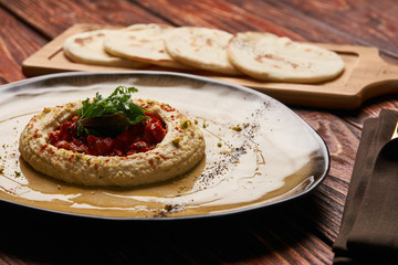 Hummus National Israeli cuisine. Hummus with harissa sauce and pistachios, close-up. Vegetarian diet food with pita bread on wooden cutting board.