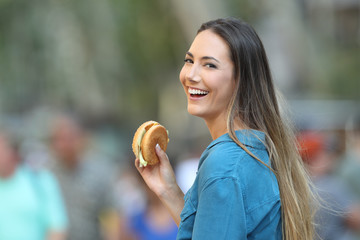 Happy woman holding a burger looking at you