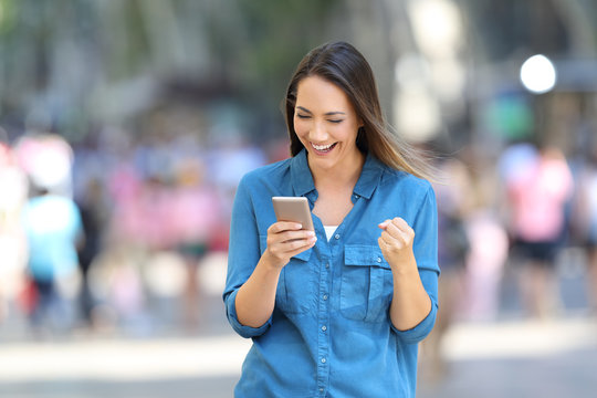 Excited woman reading good news online on the street