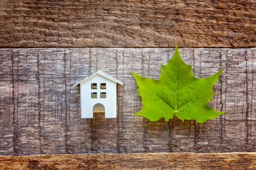 Miniature white toy model house with green maple leaf on wooden backgdrop. Eco Village, abstract environmental background. Real estate mortgage property insurance dream home ecology concept