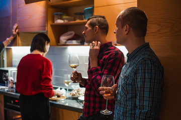 Couple of friends standing at the kitchen and drinks wine on home party