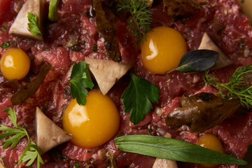 Steak tartare with egg yolk, pistachios, truffle oil, green mayonnaise on luxury porcelain plate, top view. Beef tartare chopped meat with ingredients can be used as cooking recipe or restaurant menu