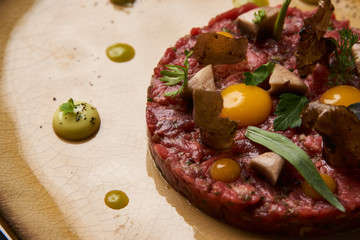 Beef tartare with egg yolk pistachios, truffle oil, green mayonnaise on luxury porcelain plate, top view, close-up