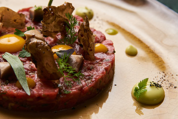 Beef tartare with egg yolk pistachios, truffle oil, green mayonnaise on luxury porcelain plate, top view, close-up