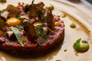 Beef tartare Steak with egg yolk, pistachios, truffle oil, green mayonnaise on porcelain plate. Classic tartare meat with ingredients. Luxury food