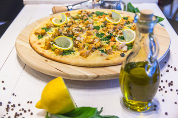 appetizing pizza with prawns, lemon, olive oil and spices on a white table