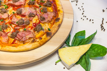 appetizing pizza with bacon, bell pepper and basil on a white table