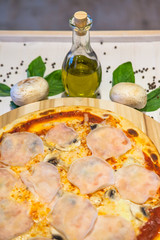 appetizing pizza with ham, basil and olive oil on a white table