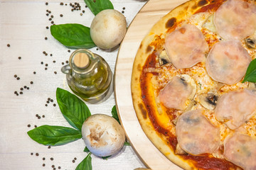 appetizing pizza with ham, basil and olive oil on a white table