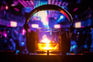 Glass with whisky with ice cube inside on dj controller at nightclub. Dj Console with club drink at...