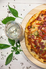appetizing pizza with small sausages, basil and a glass of white wine on a white table, flat lay