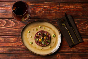 Tartare Steak with egg yolk, pistachios, truffle oil, green mayonnaise on plate and glass of red wine, served on restaurant table. Classic Beef tartare meat, Luxury food