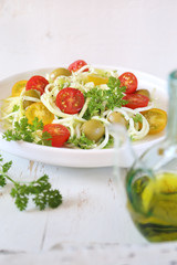 Vegetarian food: raw zucchini spaghetti salad with cherry tomatoes, olives and olive oil