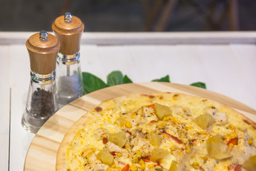 appetizing pizza with chicken and pineapple, basil and spices on a white table