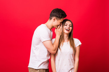 Young man telling a secret to a woman over a red background