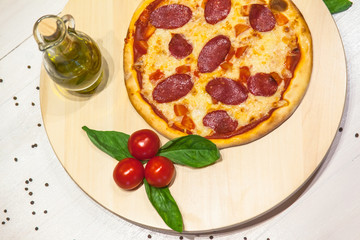 a small appetizing pizza with sausages, basil, tomatoes and olive oil on a white table