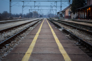 Old train station platform with its distinctive yellow safety lines on an almost abandoned electrified railway line at sunset