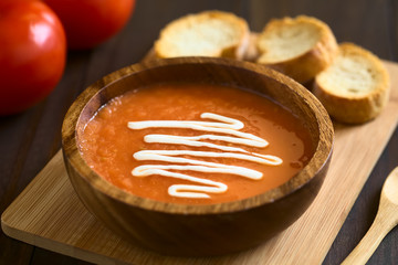 Homemade fresh cream of tomato soup served in wooden bowl with toasted bread on wooden board, photographed with natural light (Selective Focus, Focus in the middle of the soup)