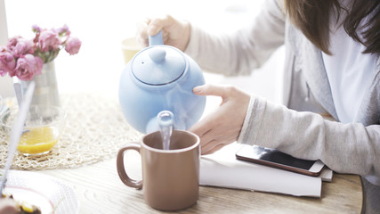 A closeup of female hands pouring hot water from a blue teapot in a cafe