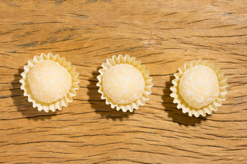 Beijinho is a candy from Brazil: condensed milk and coconut. Children brithday party sweet. Overhead of candy ball on rustic wood table.