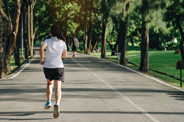 Fototapeta premium young fitness woman running in the park outdoor, female runner walking on the road outside, asian athlete jogging and exercise on footpath in sunlight morning. Sport, healthy and wellness concepts