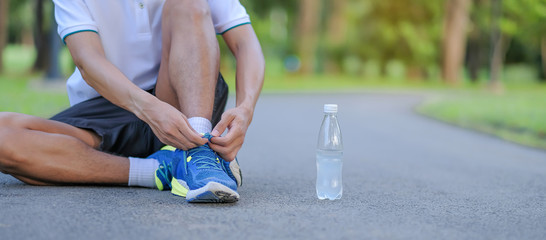 Young athlete man tying running shoes in the park outdoor, male runner ready for jogging on the...