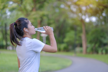 young fitness woman drinking energy water during walking in the park outdoor, female runner running on the road outside, asian athlete jogging and exercise on footpath in morning