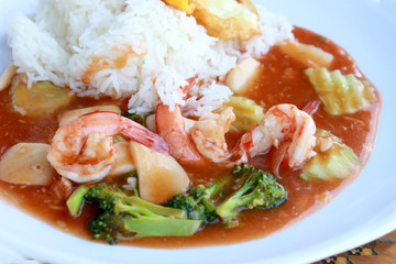 stir fried shrimp and Broccoli in thai red curry paste sauce with rice, Curry fried shrimps and cooked rice in white dish closeup on wooden table. Thai style food.