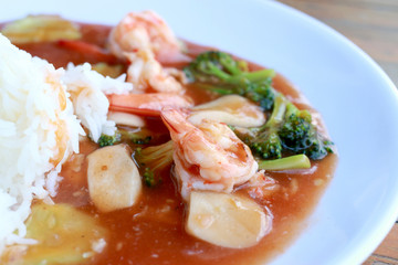 stir fried shrimp and Broccoli in thai red curry paste sauce with rice, Curry fried shrimps and cooked rice in white dish closeup on wooden table. Thai style food.