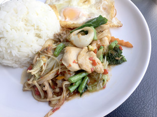 Fried spicy fried seafood with basil leaves and mixed vegetable and fried egg on jasmine rice in white dish. Thai style food.