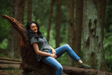 Brunette girl in jeans and in yellow glasses in the forest in summer.