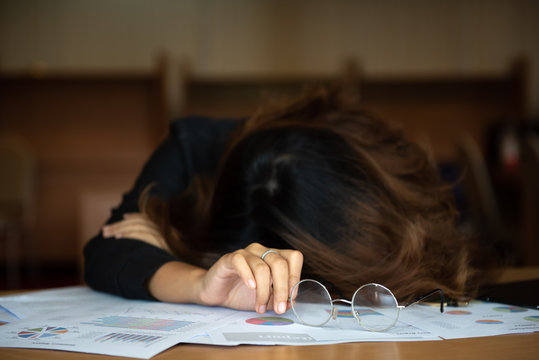 Overworked and tired businesswoman sleeping over a desk at work in her office. with a lot of paper.