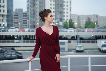 Young attractive girl in red dress. Parking and high-rise buildings in the background. Urban.