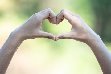 Female hands making a heart shape on natural green background.