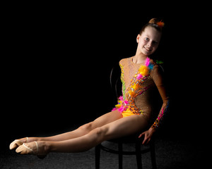 Little girl gymnast in a beautiful sporty swimsuit on a black ba